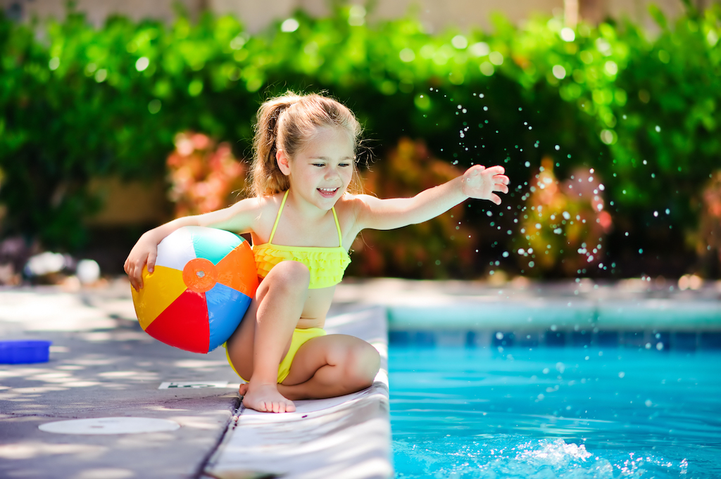 A child in a swimsuit playing with a ball in a pool